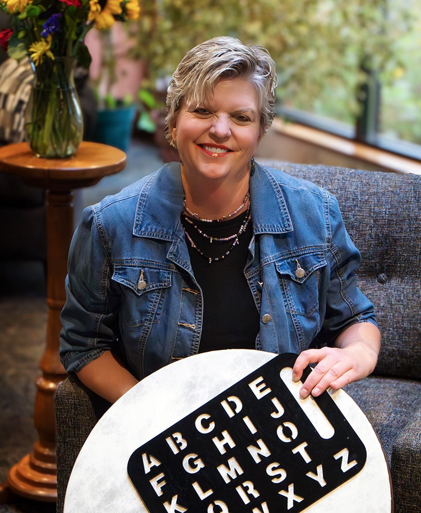 Beth Susag holding a spelling board and a drum for Neurological Music Therapy